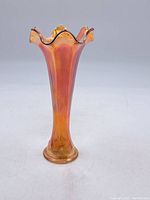 Full front view of tall iridescent orange Depression glass vase with flared ruffled top and round base.