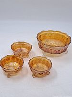Four amber Depression glass bowls - one large and three smaller, each with scalloped edges and floral designs on sides and bottom butterflies.