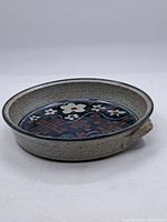 Front angled view of round pie dish showing floral pattern inside and speckled beige glaze outside.