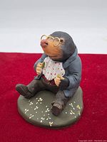 Front angle showing mole figurine seated on green base, holding objects with glasses and polka dot bib visible.
