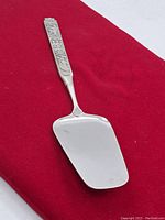 Full view of the overall cake server showing the blade and decorative handle on red background.