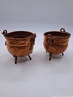 Pair of miniature copper cauldrons, each with three legs and looped handles, showing overall condition and size