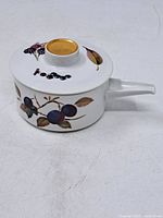 Side view of the lidded sauce boat with painted plums and grape motifs and gold accented handle on the lid.