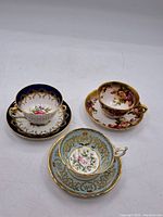 Three porcelain teacups and saucers displayed together showing their distinct patterns and gold detailing.