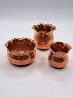 Three small copper vases on white background showing different sizes and scalloped edges.