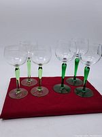Front view of all six wine glasses arranged in two sets of three on a red cloth, showing clear bowls with green stems and bases.