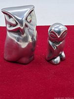 Front view of the two metallic owl sculptures showing polished aluminum surfaces with stylized facial features