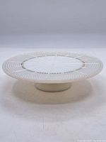 Side view of the milk glass cake tray showing its circular footed base and the decorative pattern on the surface.