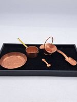 Full set of copper items displayed on black surface: Daimler tray, small pot, basket, scoop, and spoon.