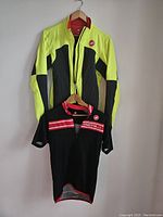 Both Castelli garments hanging on hangers: insulated Elemento jacket in yellow and black with short-sleeve black jersey underneath