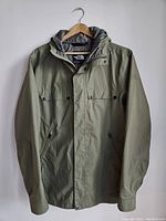Full front view of the olive green men's North Face rain jacket on a hanger, showing style and buttons.
