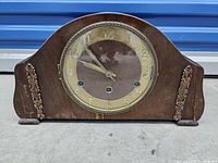 Front view showing the wooden curved case, glass clock face, and brass decorations on sides.