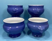 Four lavender blue Emile Henry soup bowls with lion's head accents shown from front and top angles.