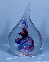 Full view of clear teardrop-shaped glass sculpture with purple and blue spiral inside on white background.