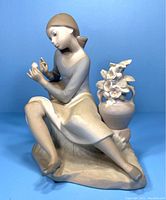 Front view of the bisque figurine showing seated girl plucking petals from flower with a floral vase nearby