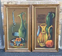 Photo showing both framed paintings side by side against a stone background.