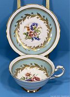 Front view of the teacup and saucer showing floral designs, gold leaf patterns, and light blue accents.