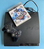 Top view of black PS3 slim console with Madden NFL 25 game case and black DualShock 3 controller on top.