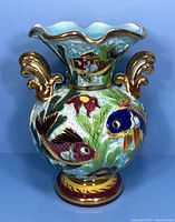 Front view showing colorful fish and floral designs on vase with gold handles and scalloped rim