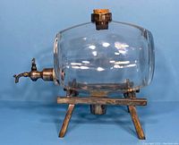 Front angled view of the clear glass whiskey barrel decanter mounted on a metal base with spigot and cork stopper. Shows shape, construction, and metal patina.