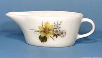 Side view of white ceramic gravy boat with yellow and white floral pattern and handle.