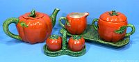 Full set front view showing teapot, creamer, sugar container, salt and pepper shakers, and green leaf tray against blue background