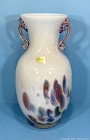 Front view of white iridescent Murano vase with label and millefiori decoration on base, showing one handle.