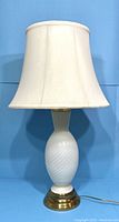 Front view of the white Murano glass lamp with brass base and fabric lampshade, shown against blue background.