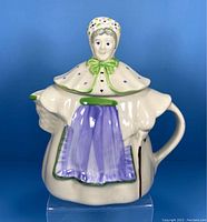 Front view of vintage ceramic teapot shaped as a granny figure with detailed painted face, bonnet, green collar, purple apron, and flowing dress-shaped body