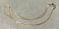 Full view of the 3-strand gold chain bracelet on a gray background showing length and style.