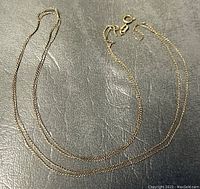 Full view of thin 10K gold rope chain laid on dark surface