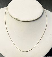 Full view of delicate gold chain necklace on white display bust showing overall length and style.