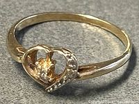 Close-up photo of gold ring with heart-shaped design and small gemstones, showing front view.