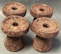 Four tapered pottery candleholders with rough lava glaze texture, dark brown in color, arranged side by side on a grey surface.