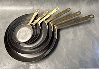 Top down view showing the set of six nesting copper pans with brass handles arranged by size.