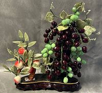 Front view showing green and dark purple grape clusters and peach branch on a wooden base.