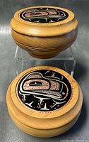 Pair of closed round wooden trinket boxes with Haida design copper and metal inlaid lids on display, showing top and side views.