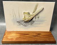 Front view of handcrafted photo art titled 'The Frog' featuring frog figure extending from picture, mounted on wood base marked 'Canada'.