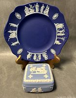 Full shot of vintage Wedgwood jasperware plate displayed on a stand with blue lidded trinket box in front.