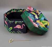 Gold wishbone bar pin with attached long pin and paperboard box with flamingo and floral print, box lid removed and placed at angle.