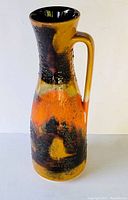 Photo showing the front view of the West German pottery ewer with orange-black-brown fat lava glaze and elongated handle.