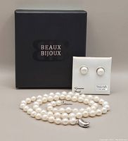 Lot components including the black 'Beaux Bijoux' box, pearl necklace arranged in a circle, and earrings on a white card labeled 'Genuine Pearl'.