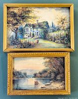 Two framed watercolour paintings side by side on a green surface. One depicts a house surrounded by trees, the other a river scene with boats, both signed M.T.