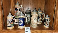 Photo showing seven traditional German ceramic beer steins with pewter lids of various sizes from approximately 6 to 12 inches tall. The largest is a music box stein with a sculpted lid.