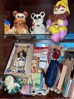 Top shelf displaying ceramic teddy bears, a ceramic garden gnome, boxed doll, and small decorative items.