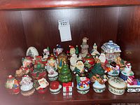 Wide view showing a group of 28 Christmas-themed hinged trinket boxes on a wooden shelf featuring various characters and holiday symbols.