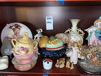 Shelf displaying various collectibles including ceramic figurines, decorative plate, painted eggs, ceramic vase, and small figurines