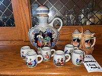 Full overview of the decanter, small mugs, and beer stein salt and pepper shakers on wood surface with cabinet background