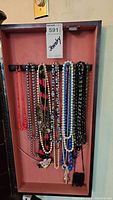 Photo of multiple long beaded necklaces hanging inside a jewelry case, showing variety of colors and styles.