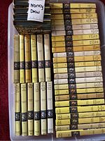 Full view of 44 Nancy Drew books arranged in two bins showing yellow hardcovers and various spine titles.